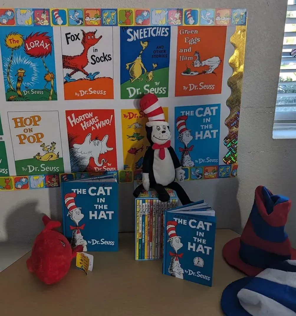 A cat in the hat is sitting on a table in front of a window.