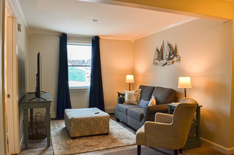 A living room with a couch , chair , ottoman and television.