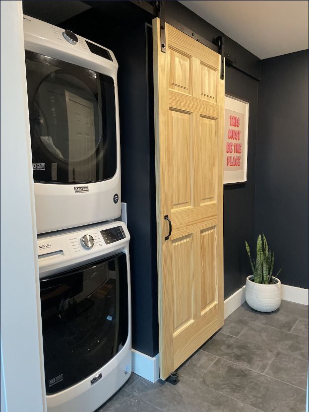 A laundry room with a stacked washer and dryer and a sliding barn door