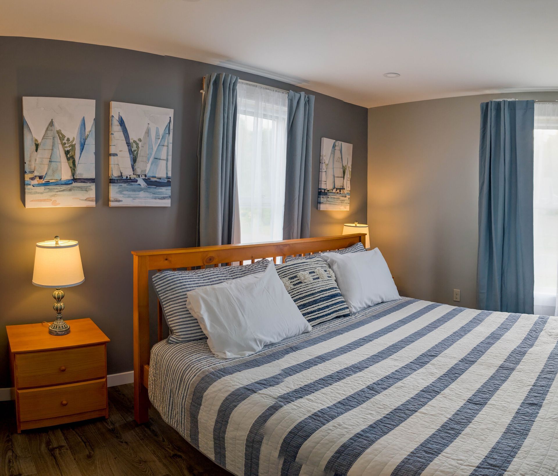 A bedroom with a bed , nightstand , lamp and paintings on the wall.