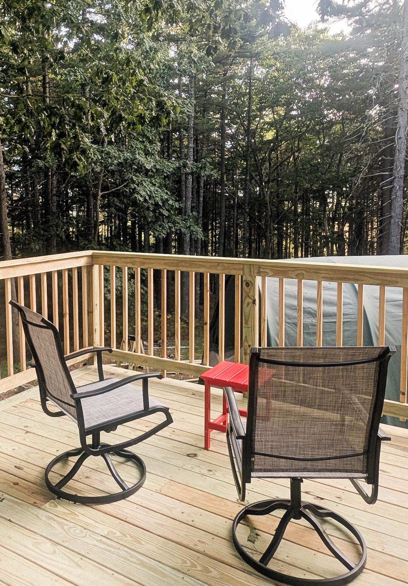 Two swivel chairs on a wooden deck, with a red side table, overlooking a forest.
