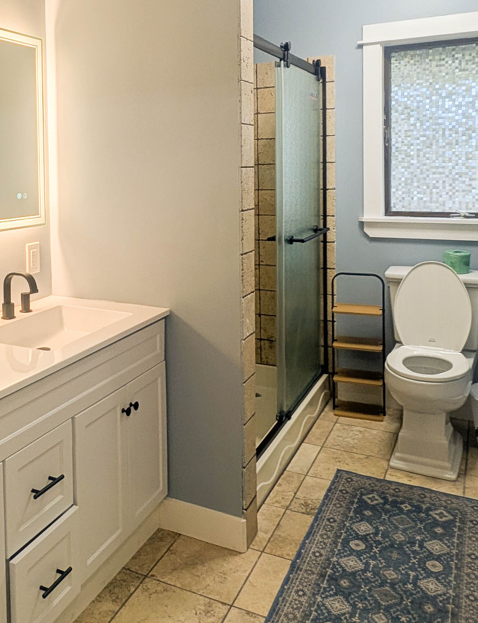Bathroom with white vanity, glass shower, toilet, and blue rug.