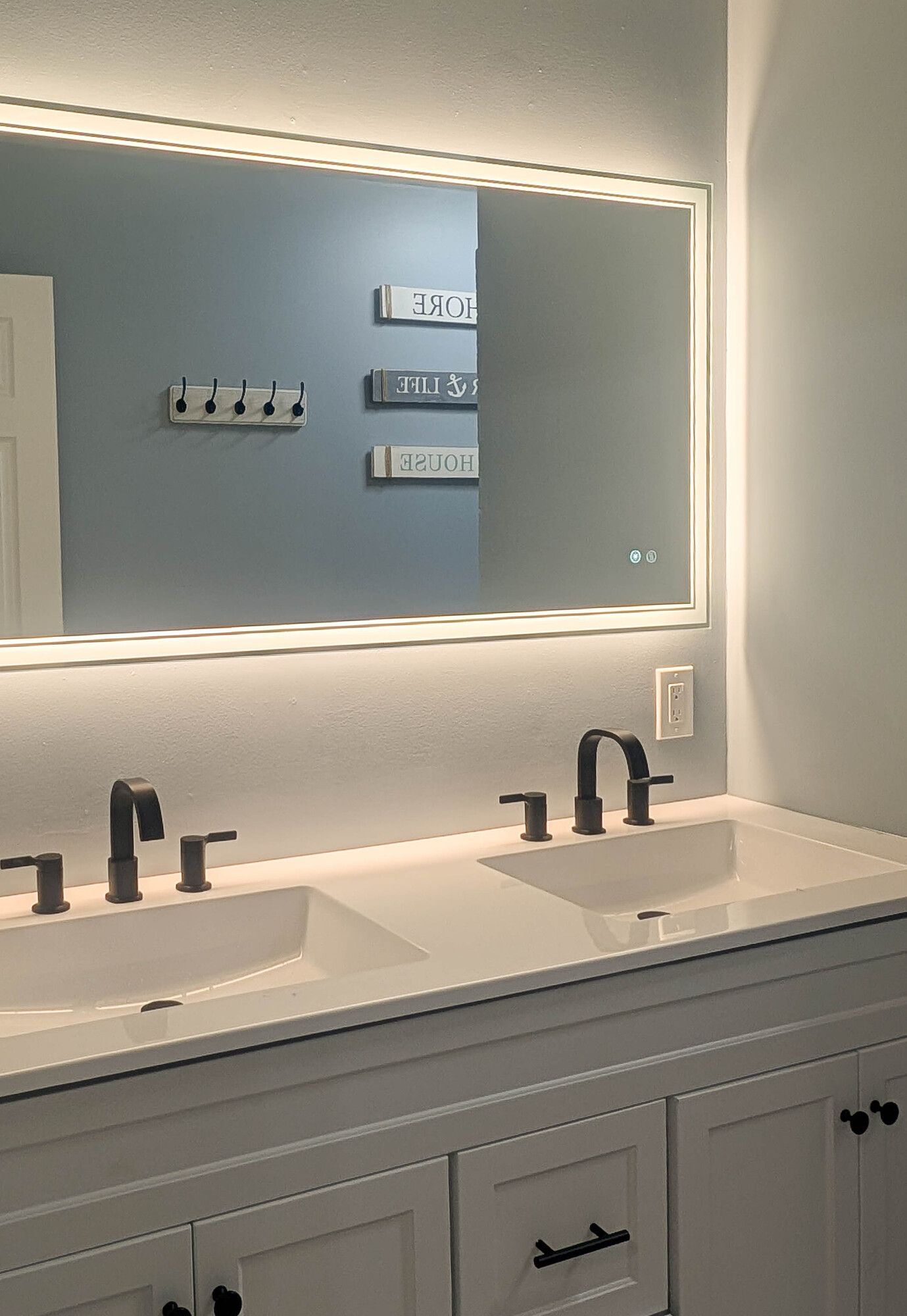 Bathroom with a lighted mirror over a double sink vanity with black fixtures.