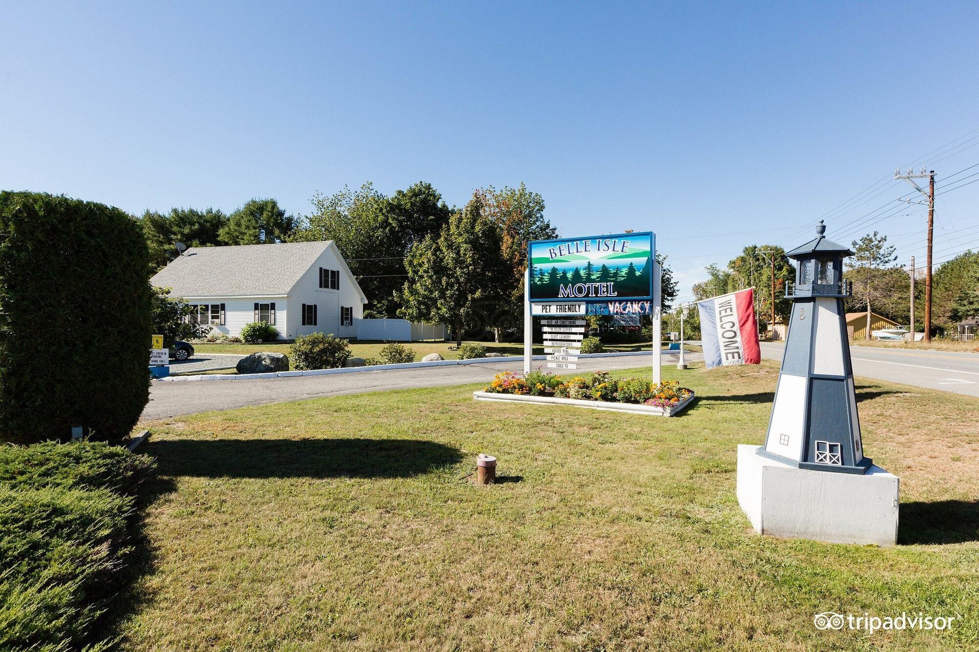 A lighthouse is in the middle of a grassy field next to a sign.