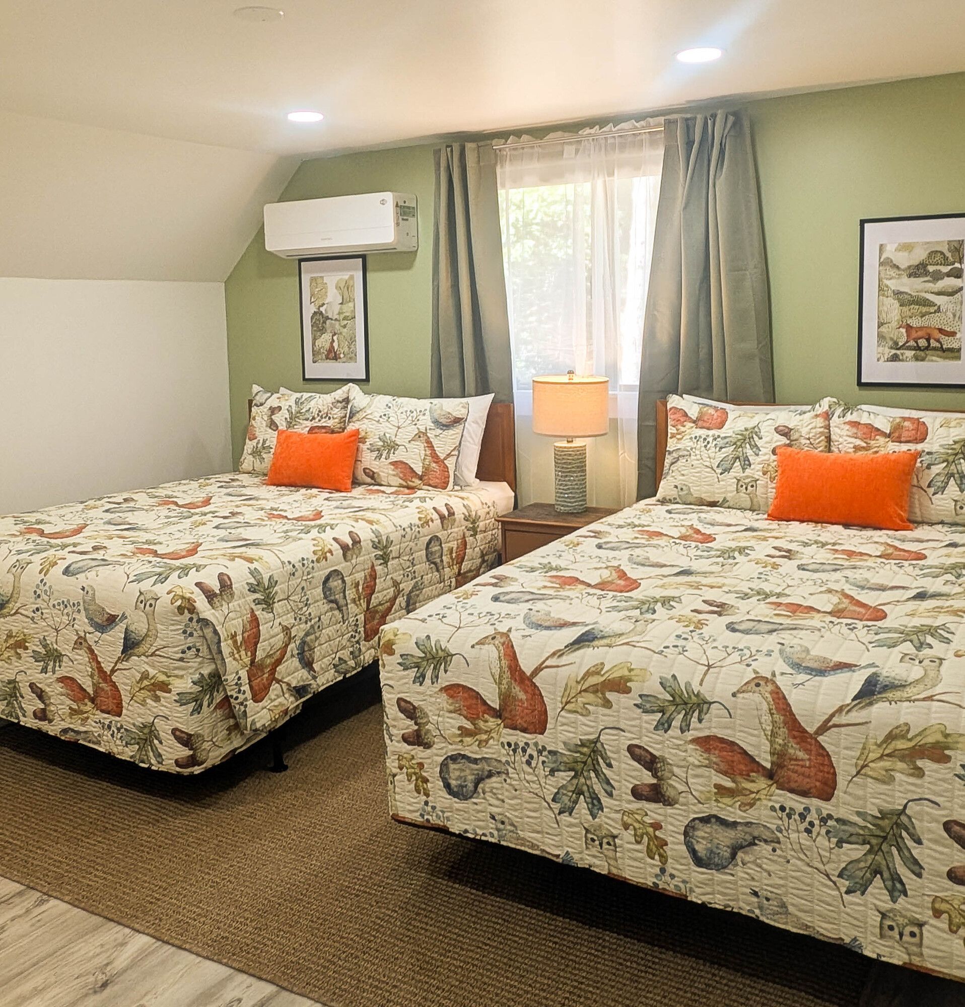 Two queen beds in a green-walled room with matching floral bedding, orange pillows, and artwork.