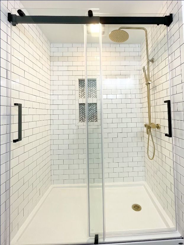 A shower with white tiles and a sliding glass door.