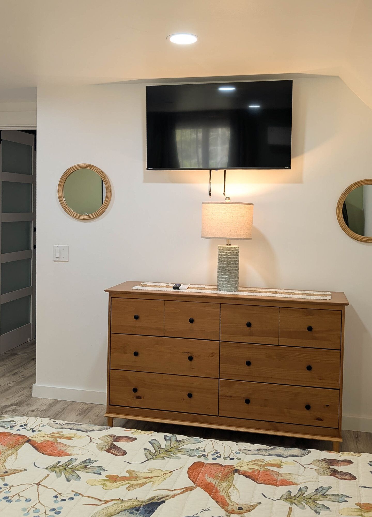 Bedroom with a wood dresser, a TV, two round mirrors, and a colorful rug.