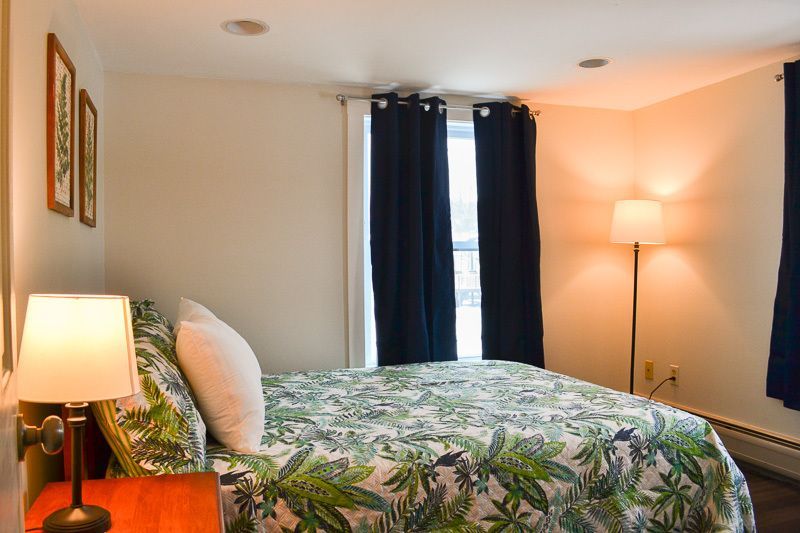 A bedroom with a bed , lamp , nightstand and window.