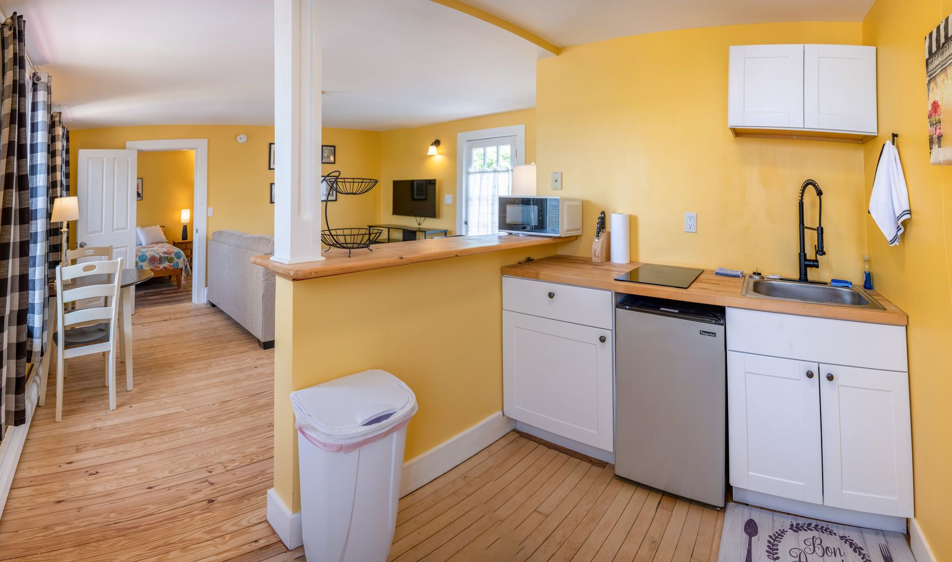 A kitchen with yellow walls and white cabinets and a trash can
