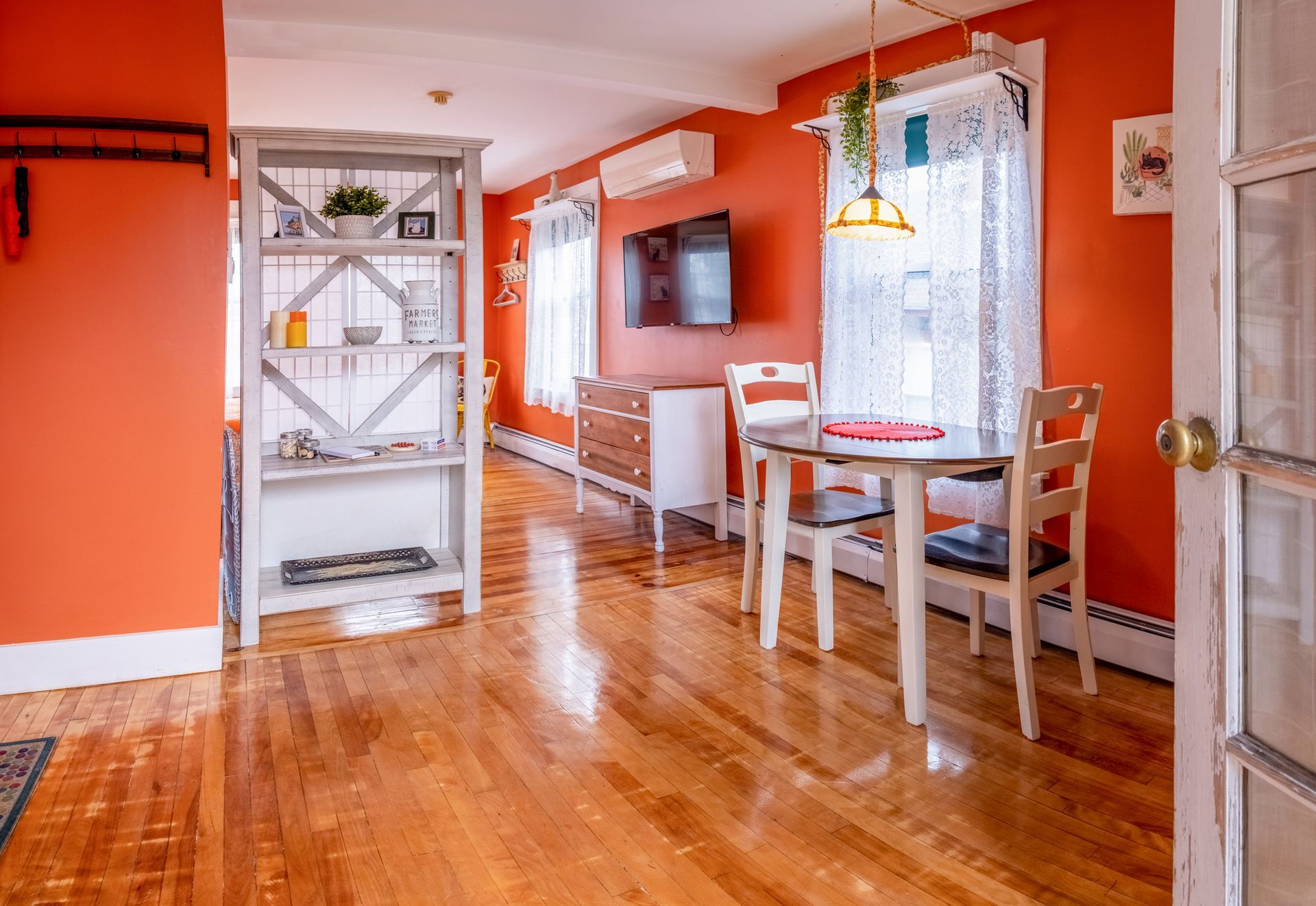 A living room with orange walls , hardwood floors , a table and chairs.