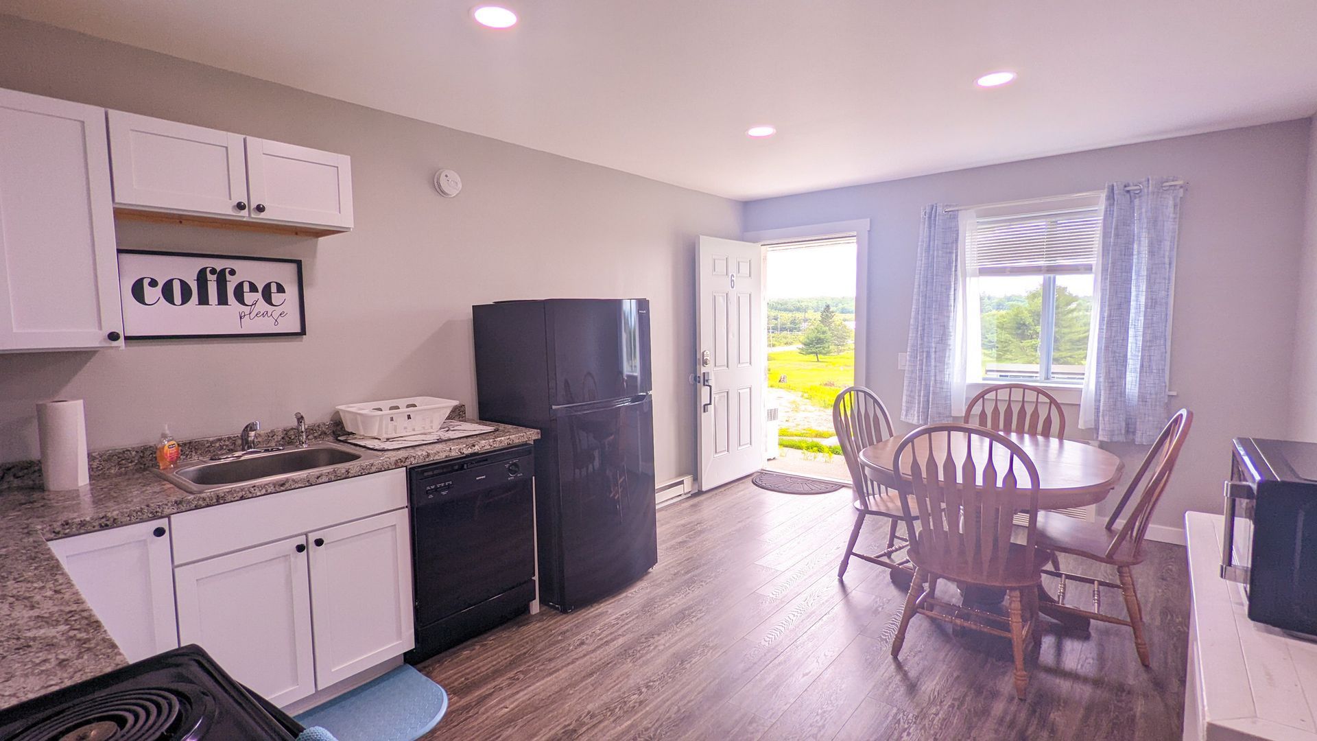 A kitchen with white cabinets , a black refrigerator , a table and chairs.