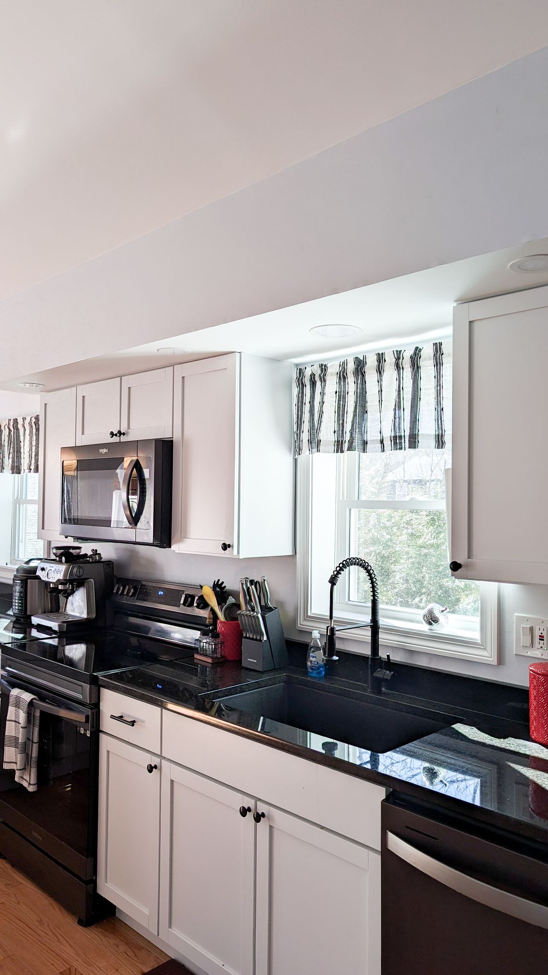 A kitchen with white cabinets , black counter tops , stainless steel appliances and a window.