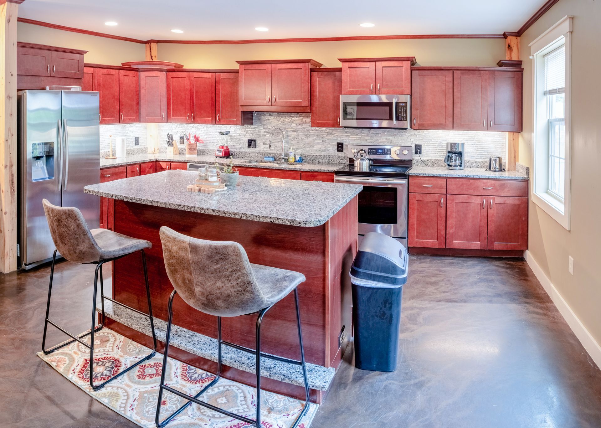 A kitchen with red cabinets , granite counter tops , stainless steel appliances and a large island.