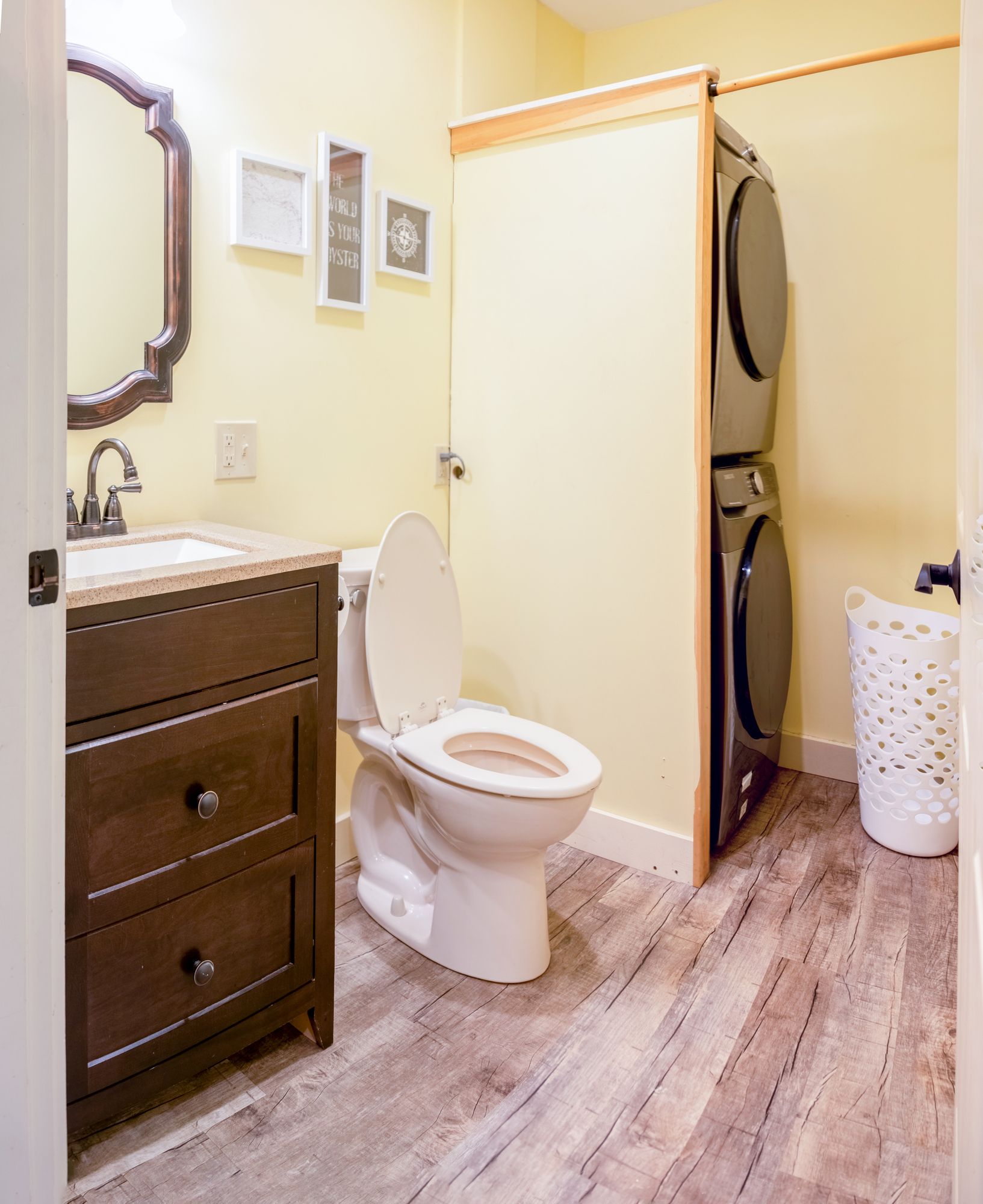A bathroom with a toilet , sink , mirror and washer and dryer stacked on top of each other.
