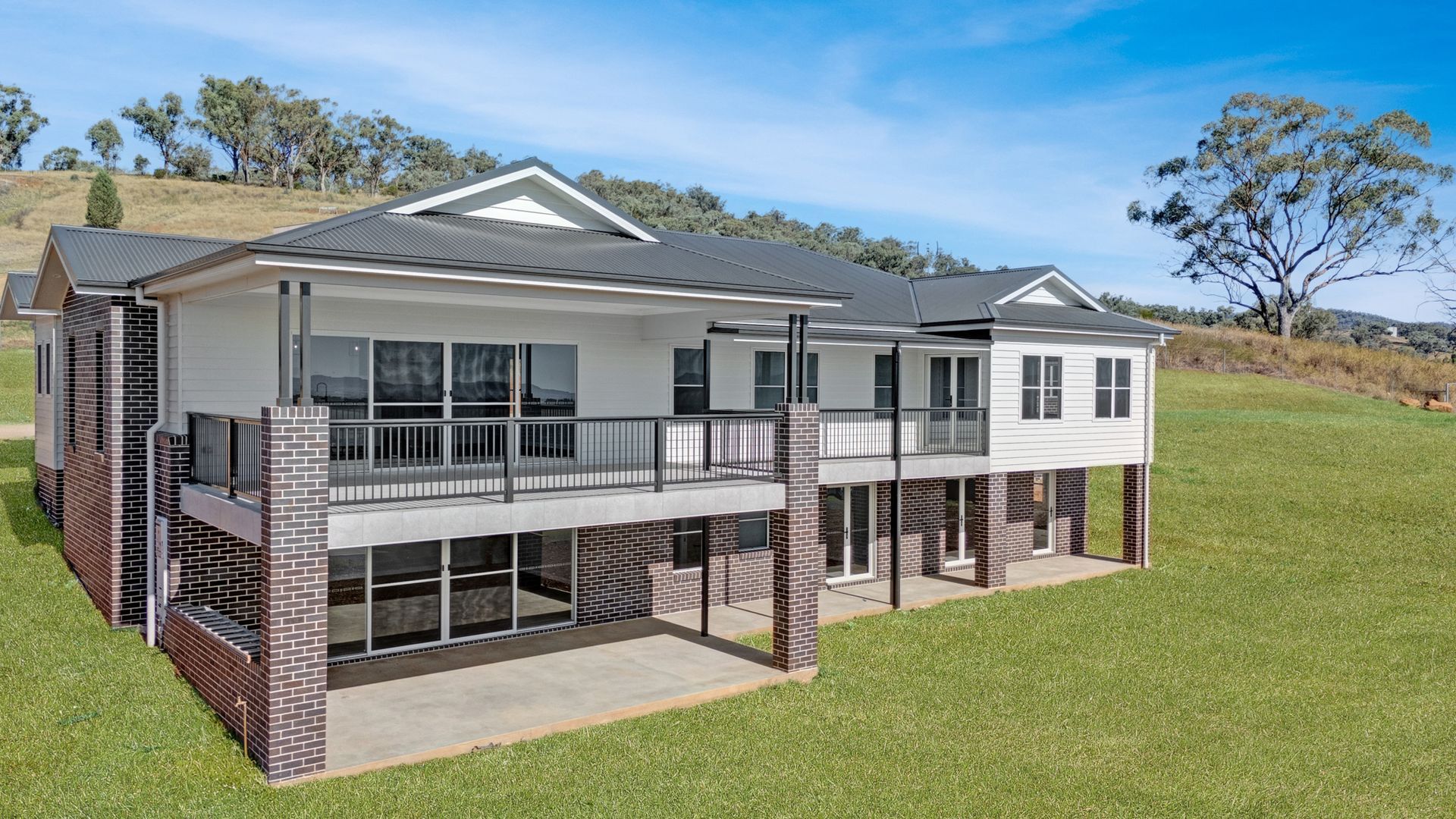 A large house with a large deck is sitting on top of a lush green field.