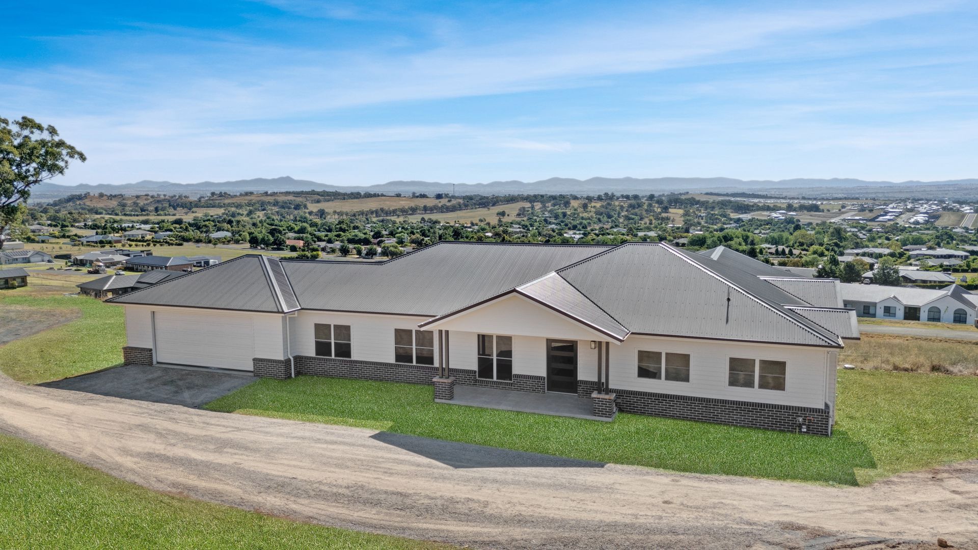 A large white house with a gray roof is sitting on top of a grassy hill.