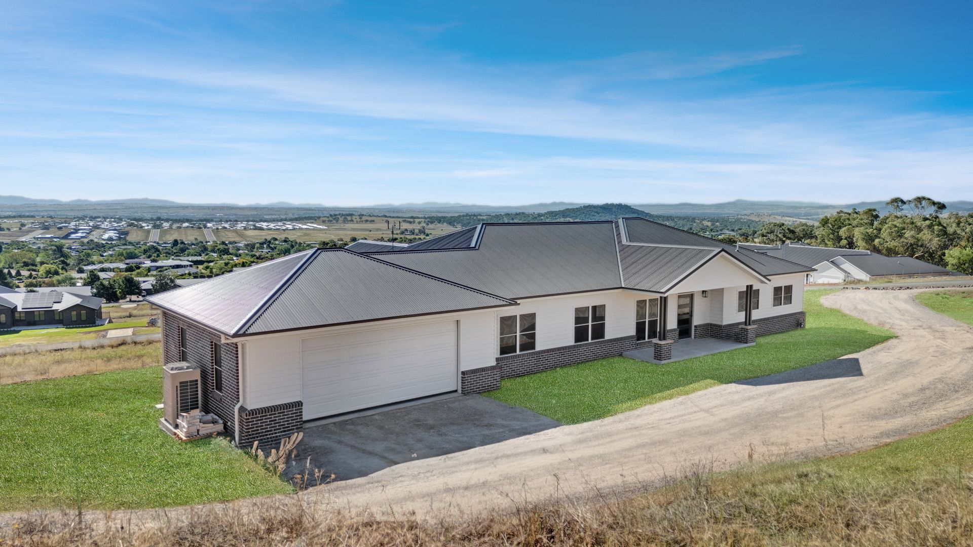 A large house is sitting on top of a grassy hill next to a dirt road.