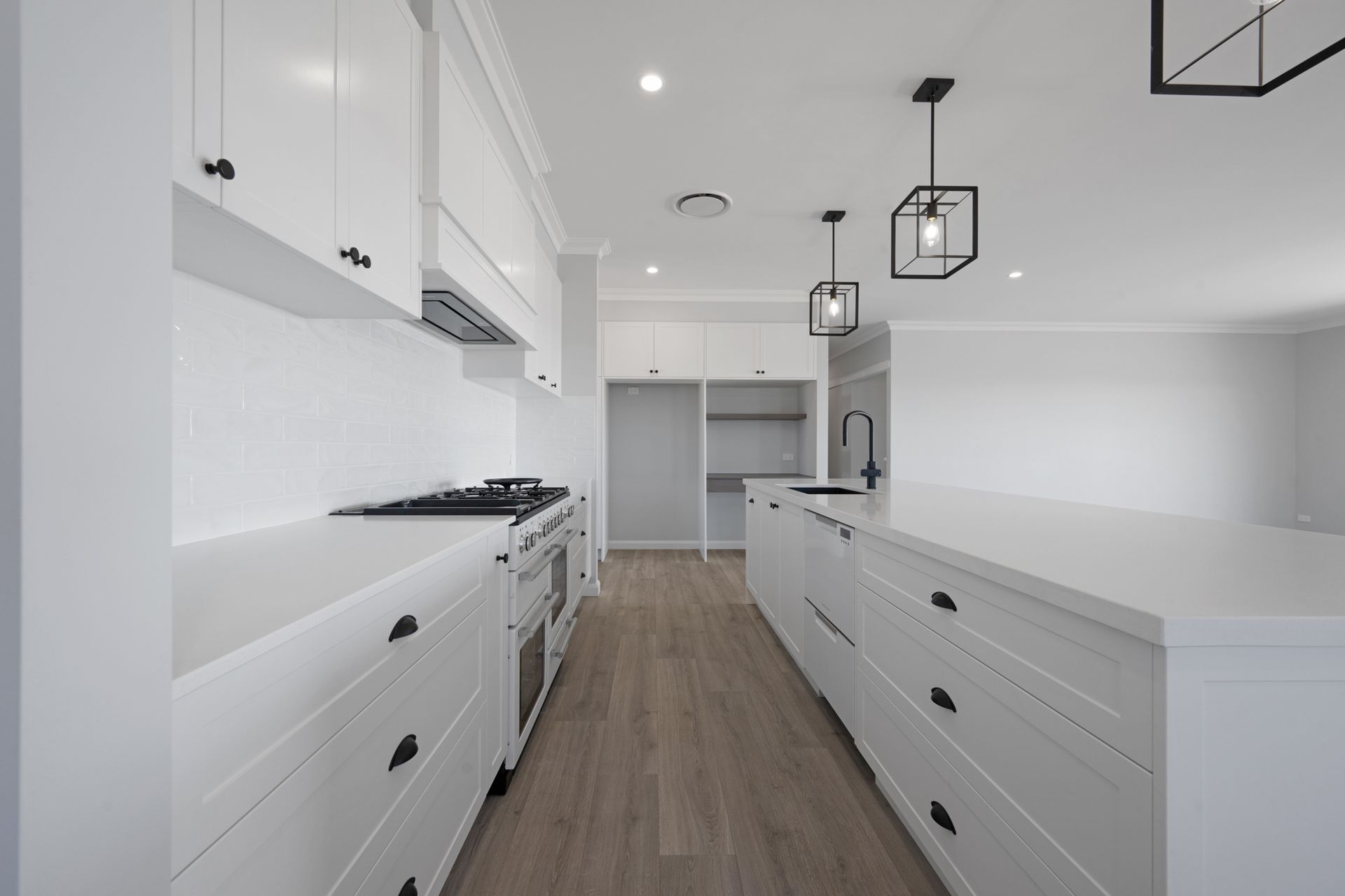 A long kitchen with white cabinets and black handles.