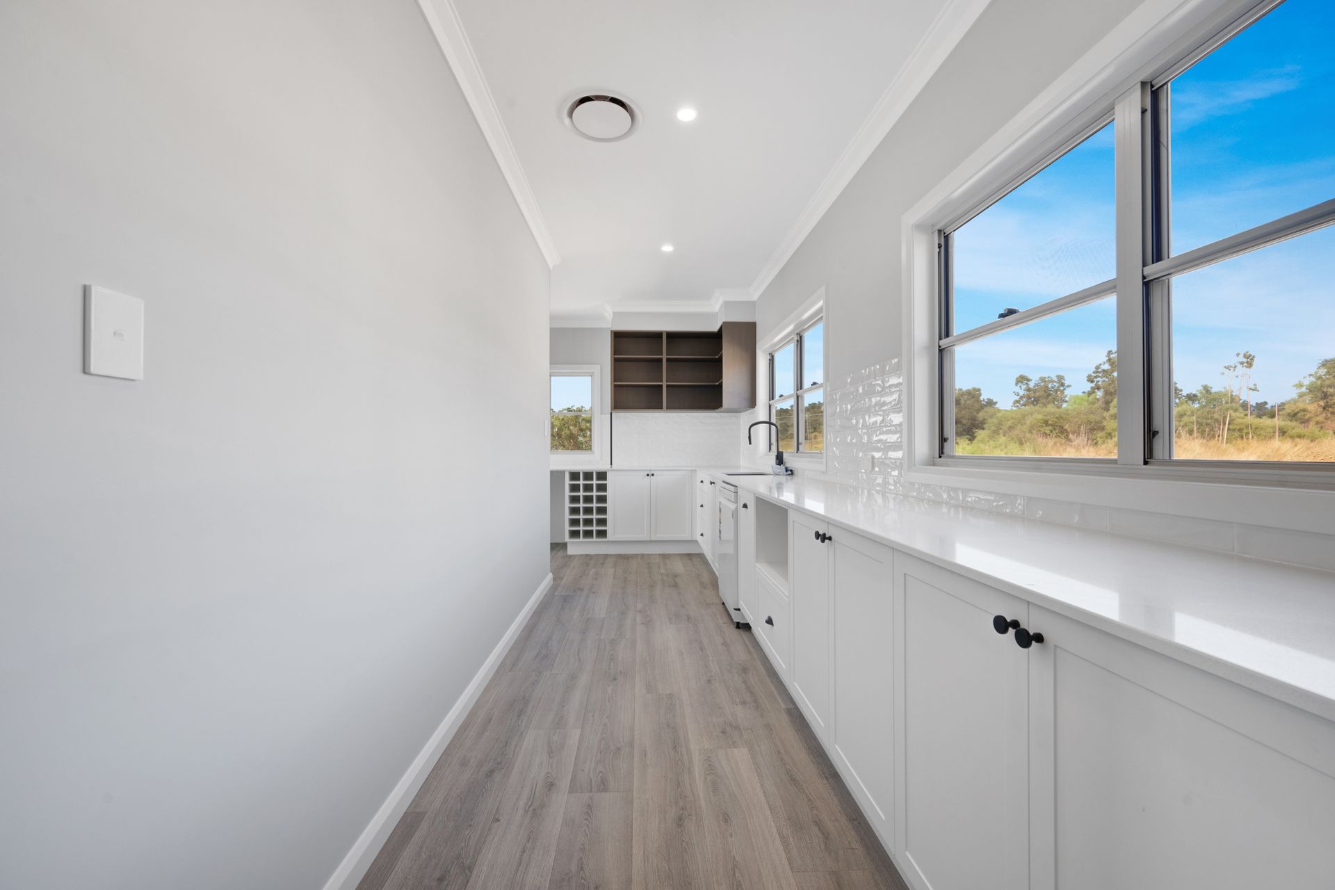 A long hallway in a kitchen with white cabinets and hardwood floors.