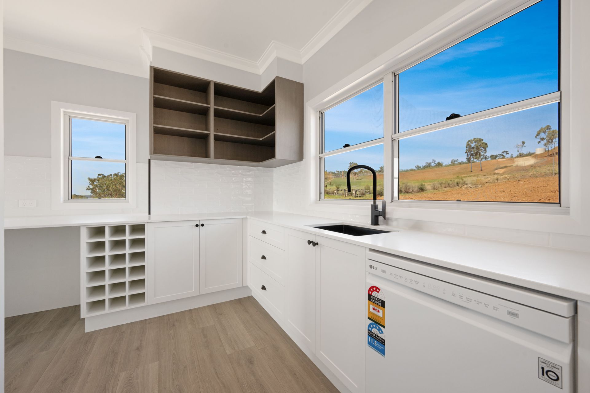 A kitchen with white cabinets , a sink , a dishwasher and two windows.