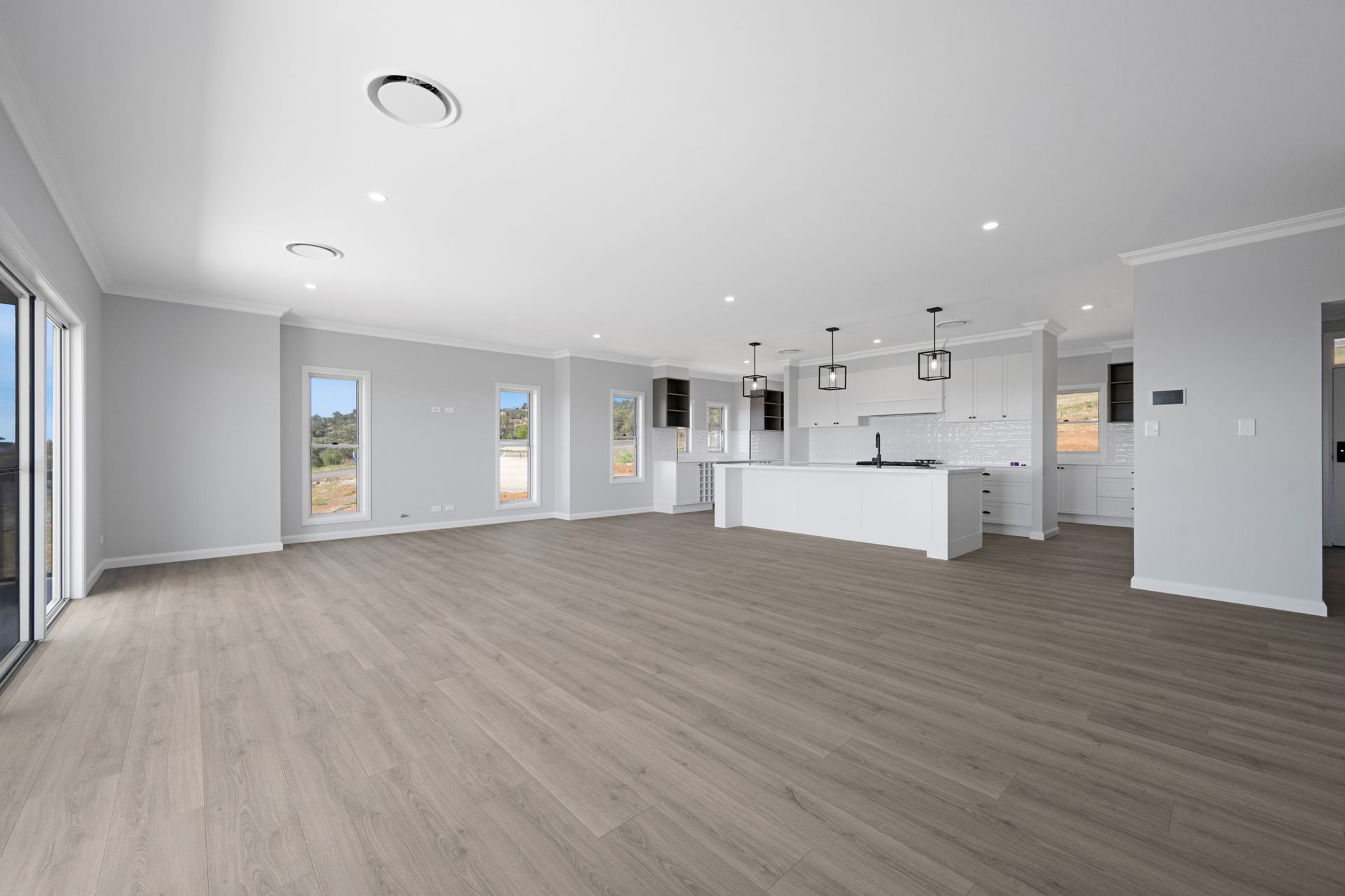 A large empty room with hardwood floors and a kitchen in the background.