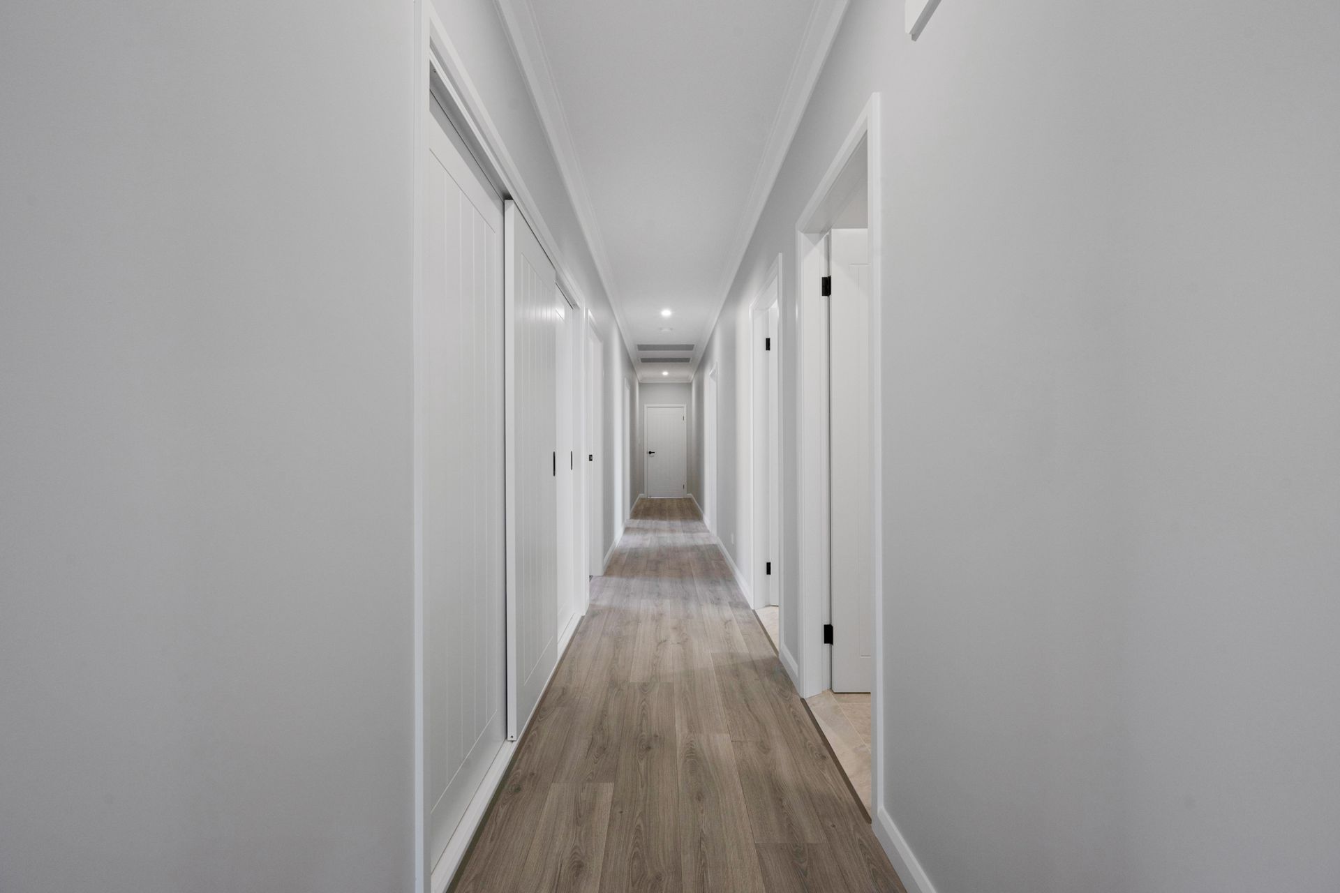 A long hallway with white walls and wooden floors in a house.