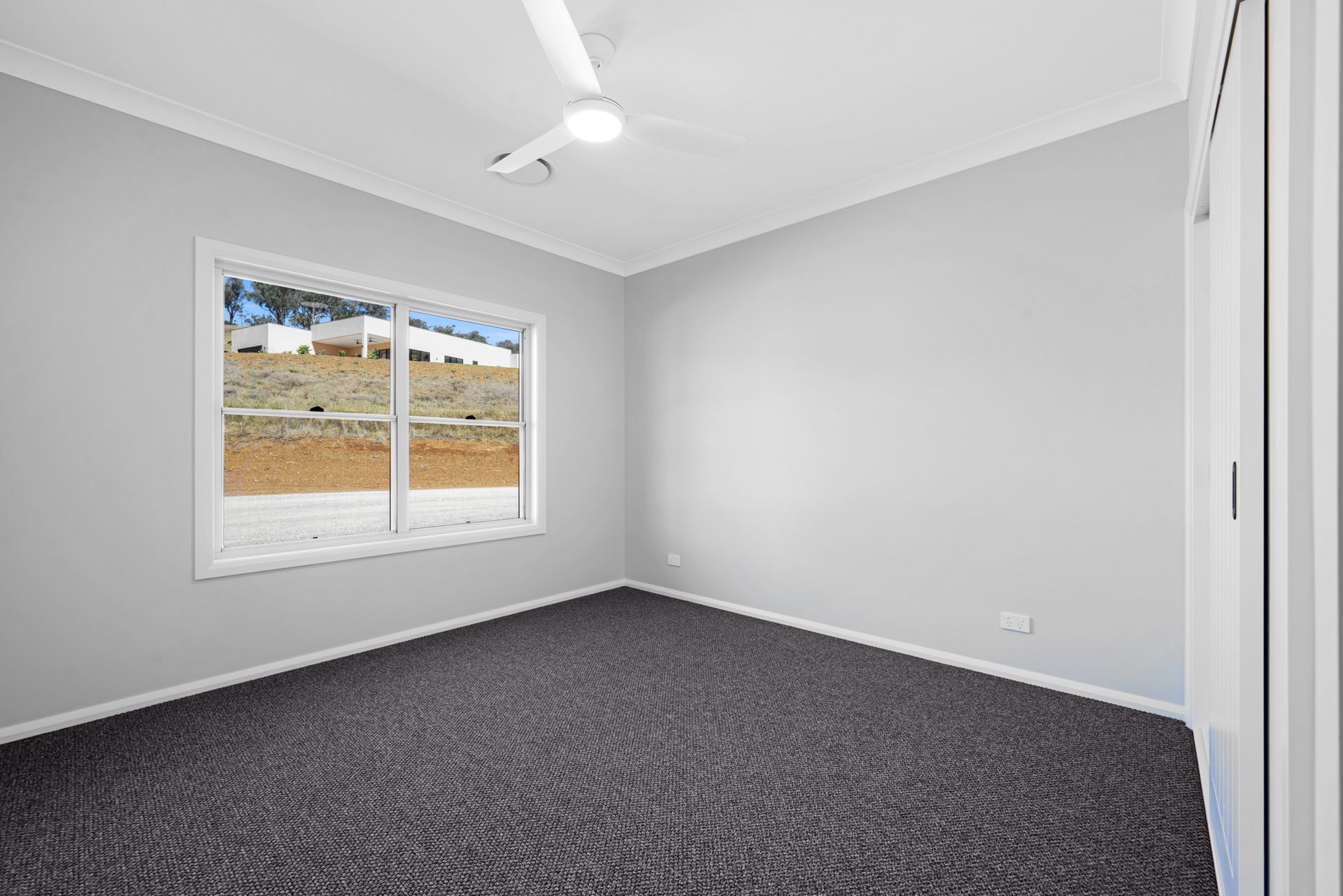 An empty bedroom with a ceiling fan and two windows.