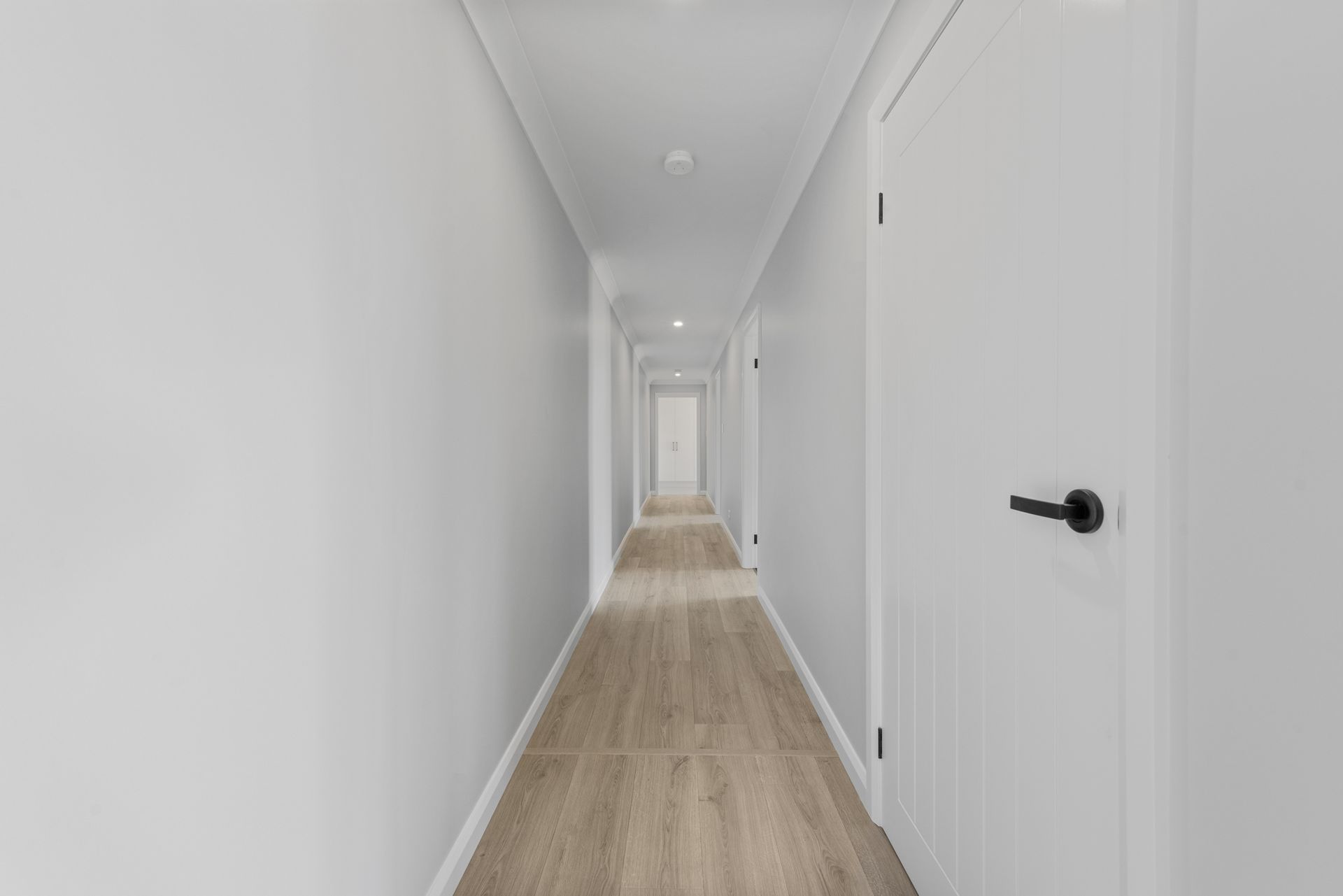 A long hallway with white walls and wooden floors in a house.
