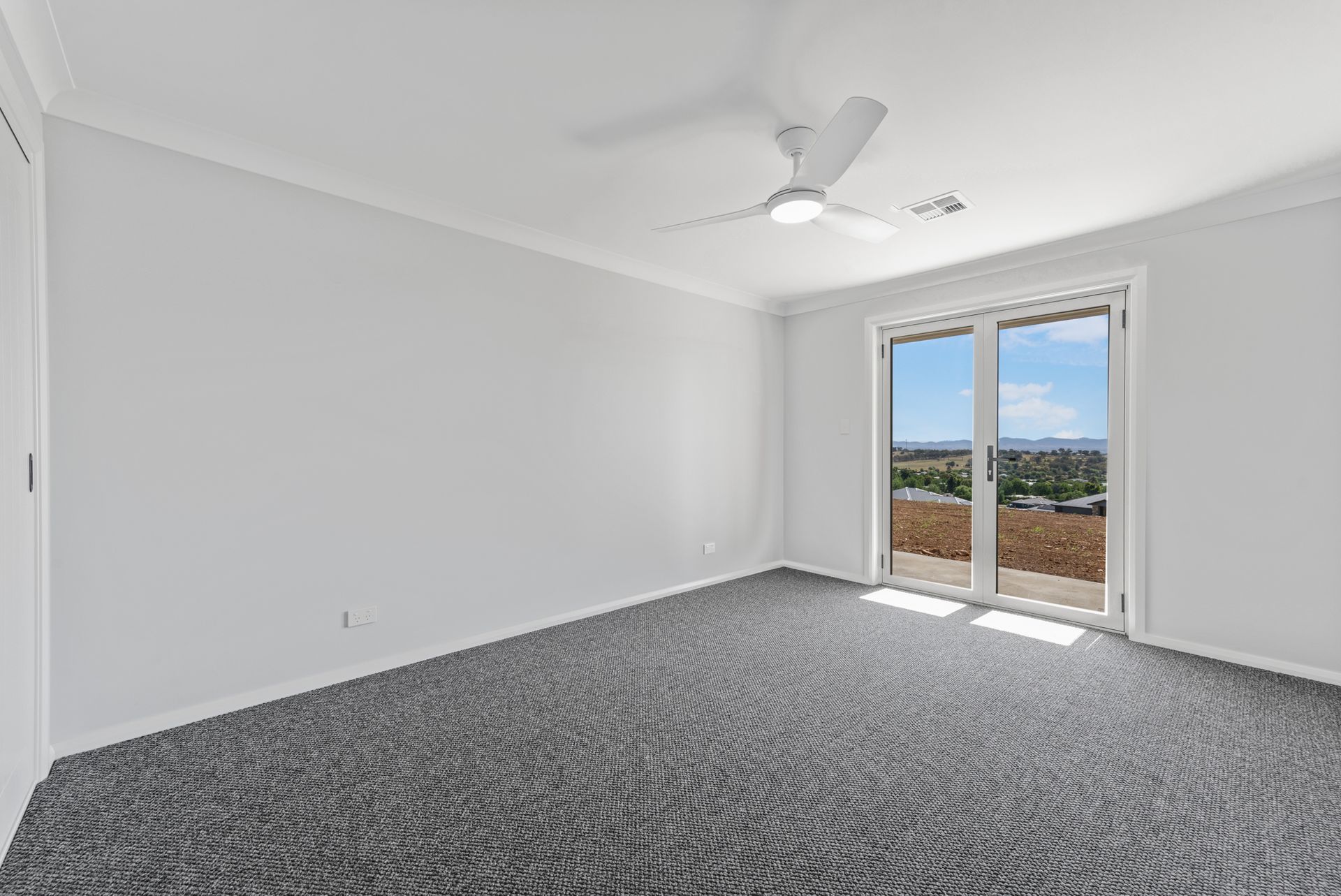 An empty room with a ceiling fan and sliding glass doors.