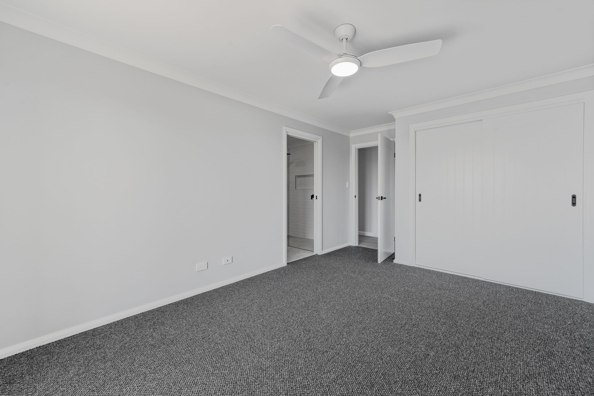 An empty bedroom with a ceiling fan and a gray carpet.