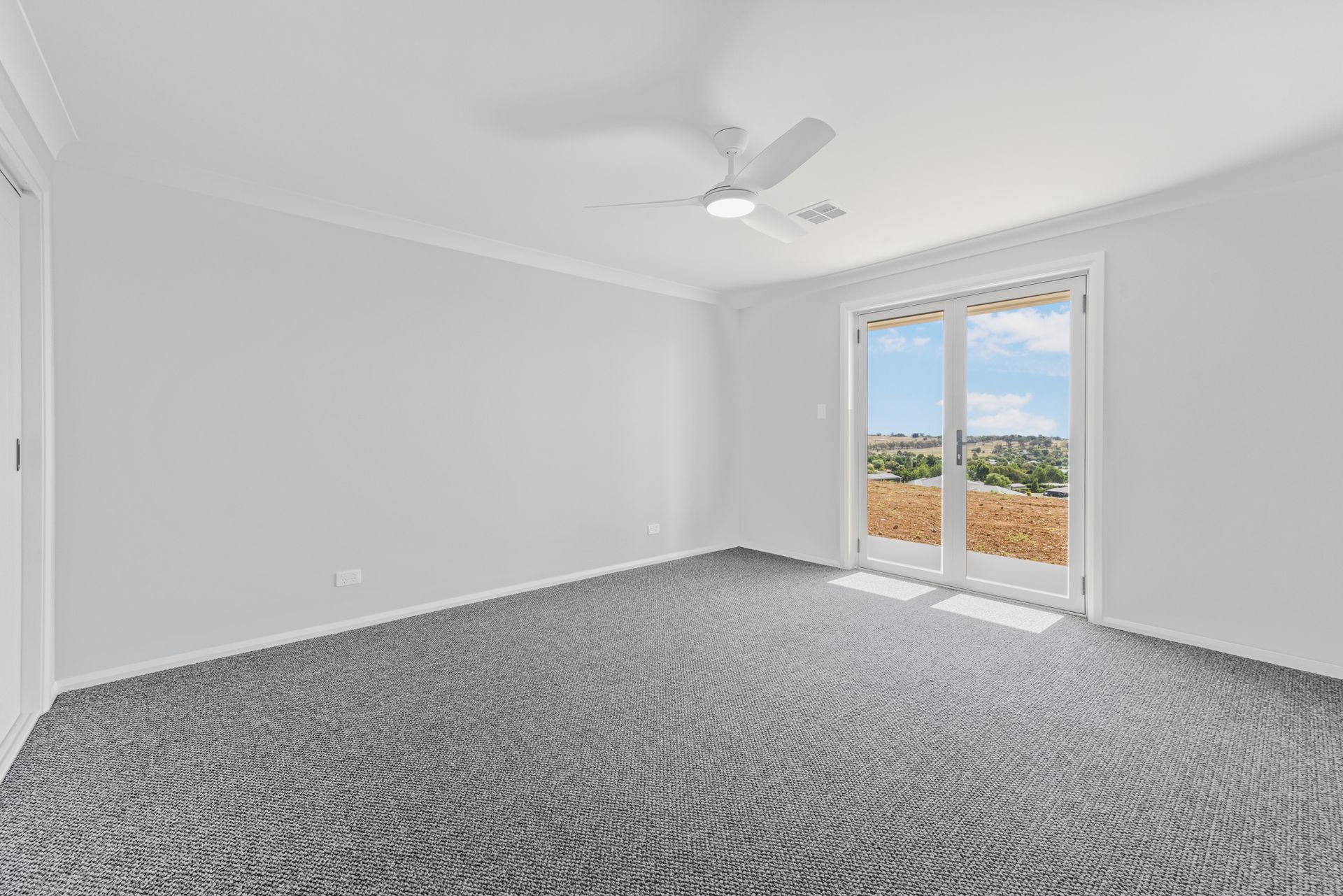 An empty room with a ceiling fan and sliding glass doors.