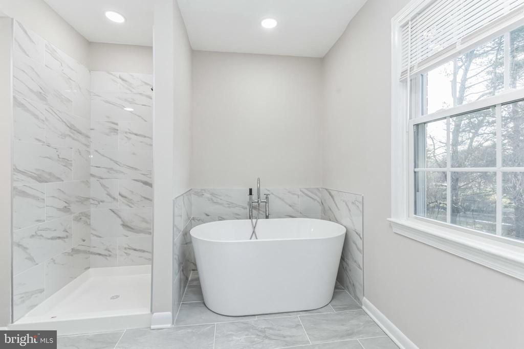 Bathroom with a white freestanding tub, marble tile shower and wall, and a window.