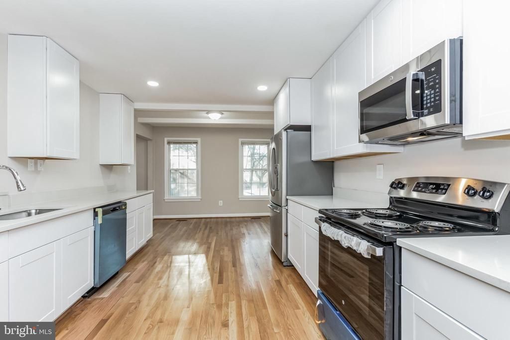 Modern kitchen with white cabinets, stainless steel appliances, and hardwood floors.