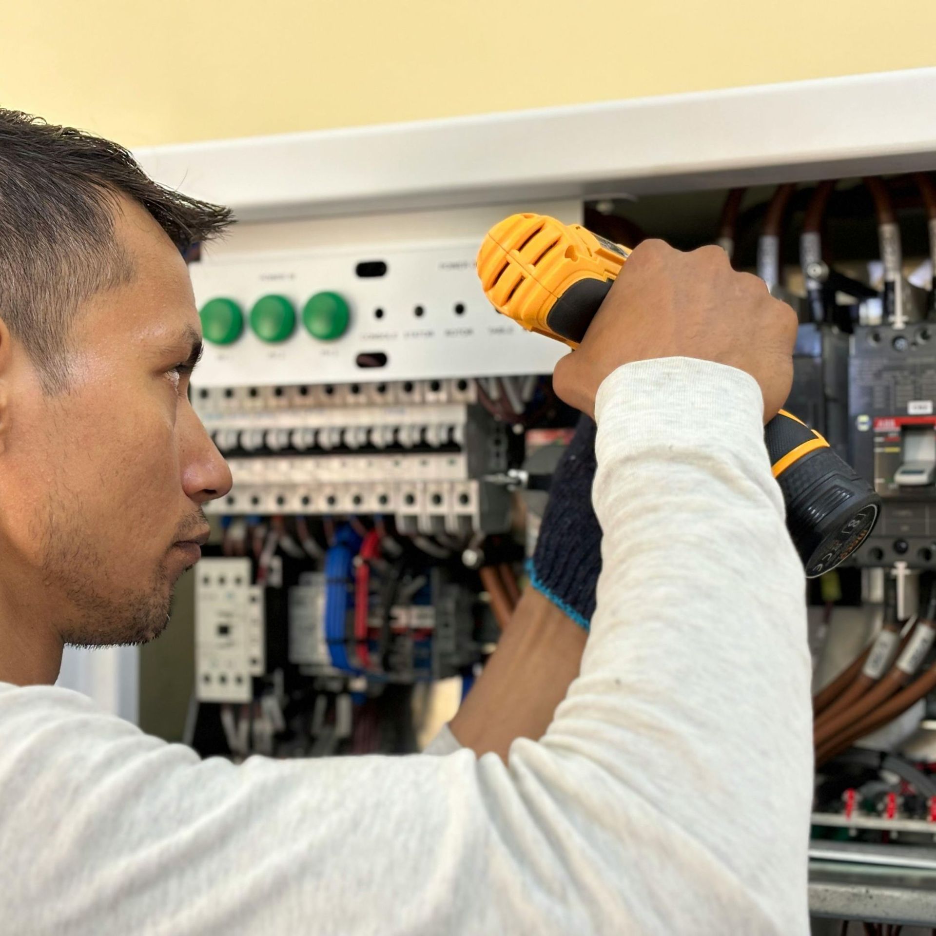 Electrician inspects wiring inside a control panel, holding a flashlight.