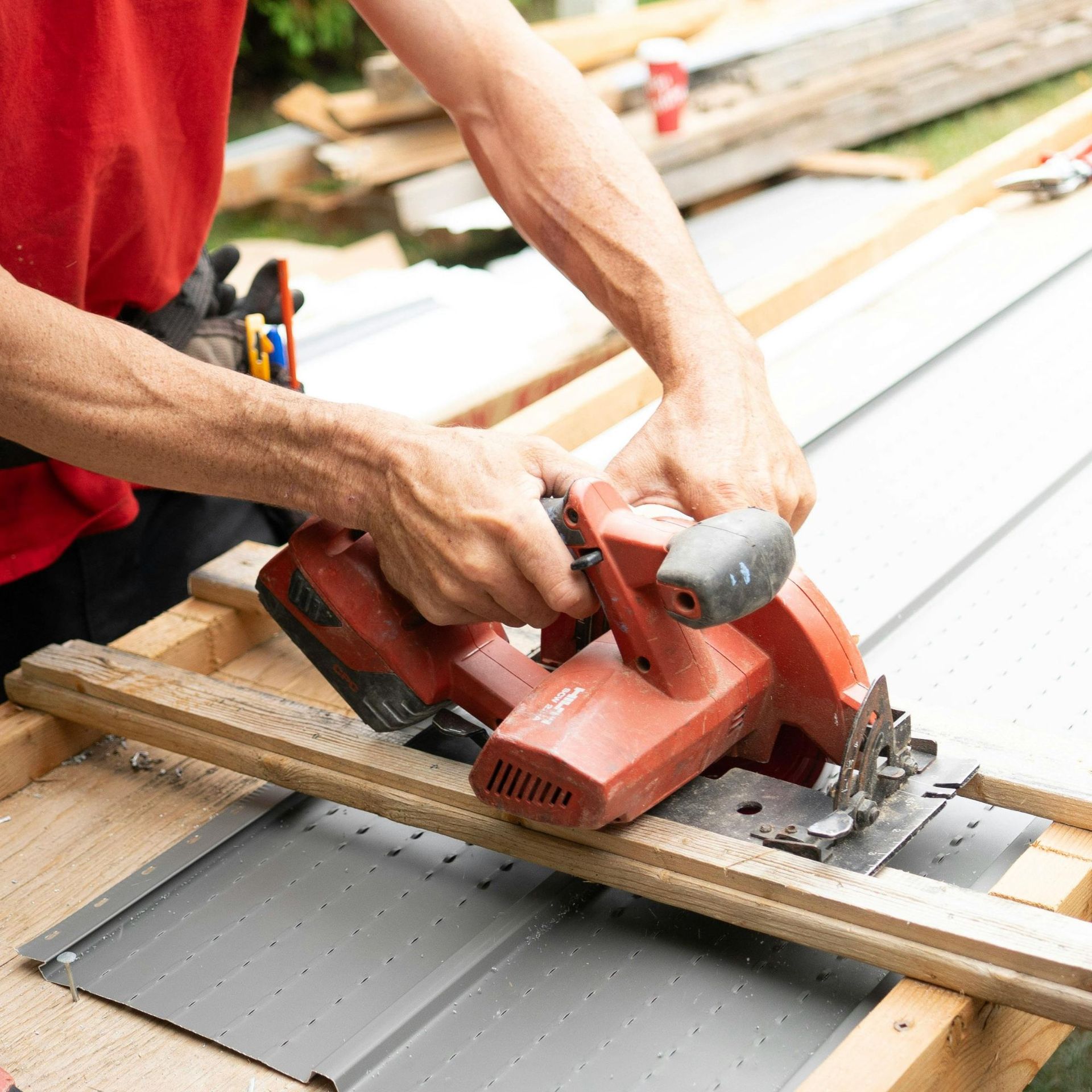 Person uses a red circular saw to cut a piece of wood on a wooden surface outdoors.