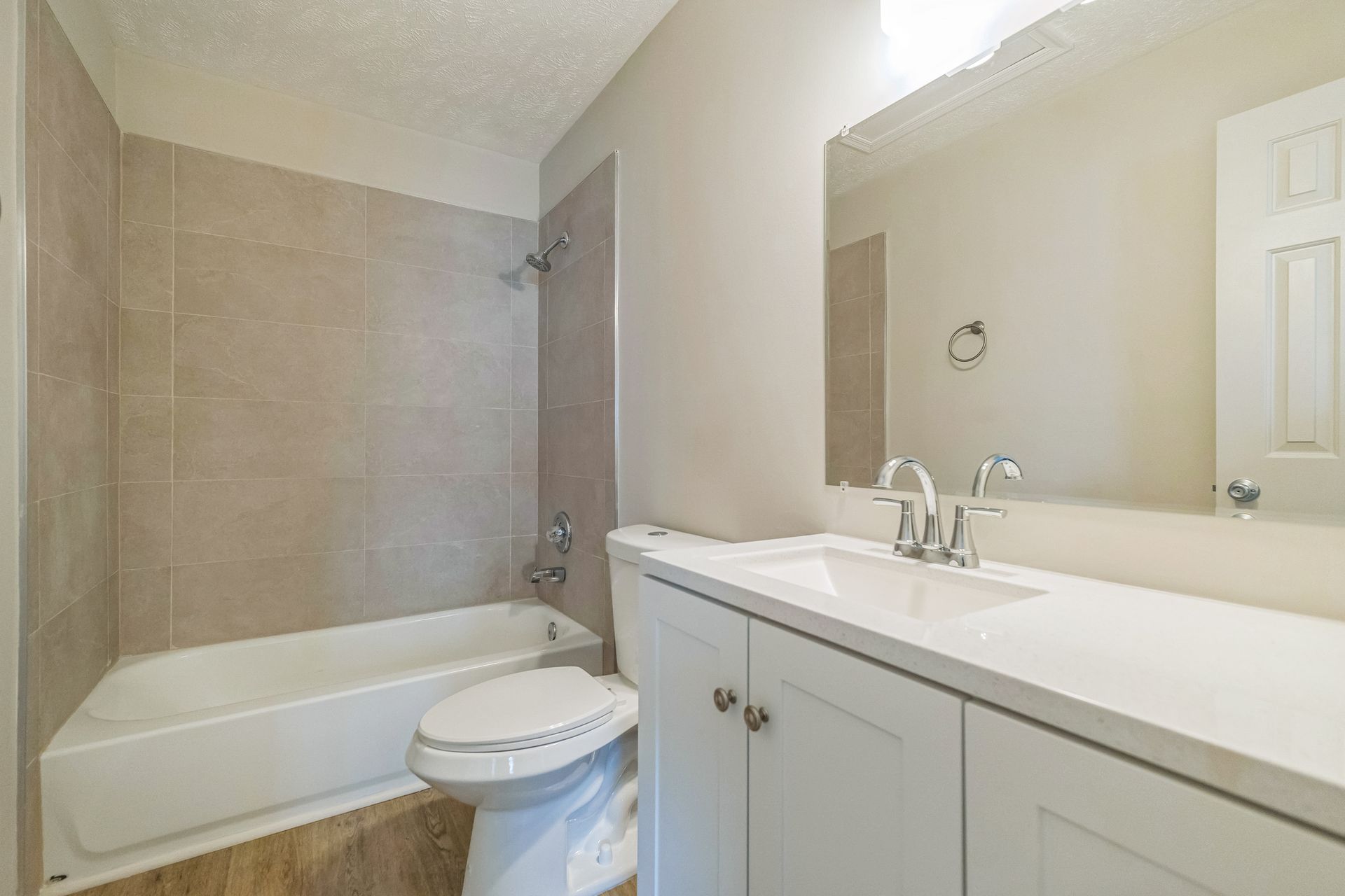 Bathroom with white vanity, toilet, bathtub/shower, and beige tiled walls.