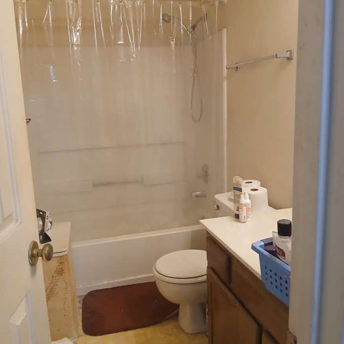 Bathroom with a white bathtub, toilet, and vanity with brown cabinetry.