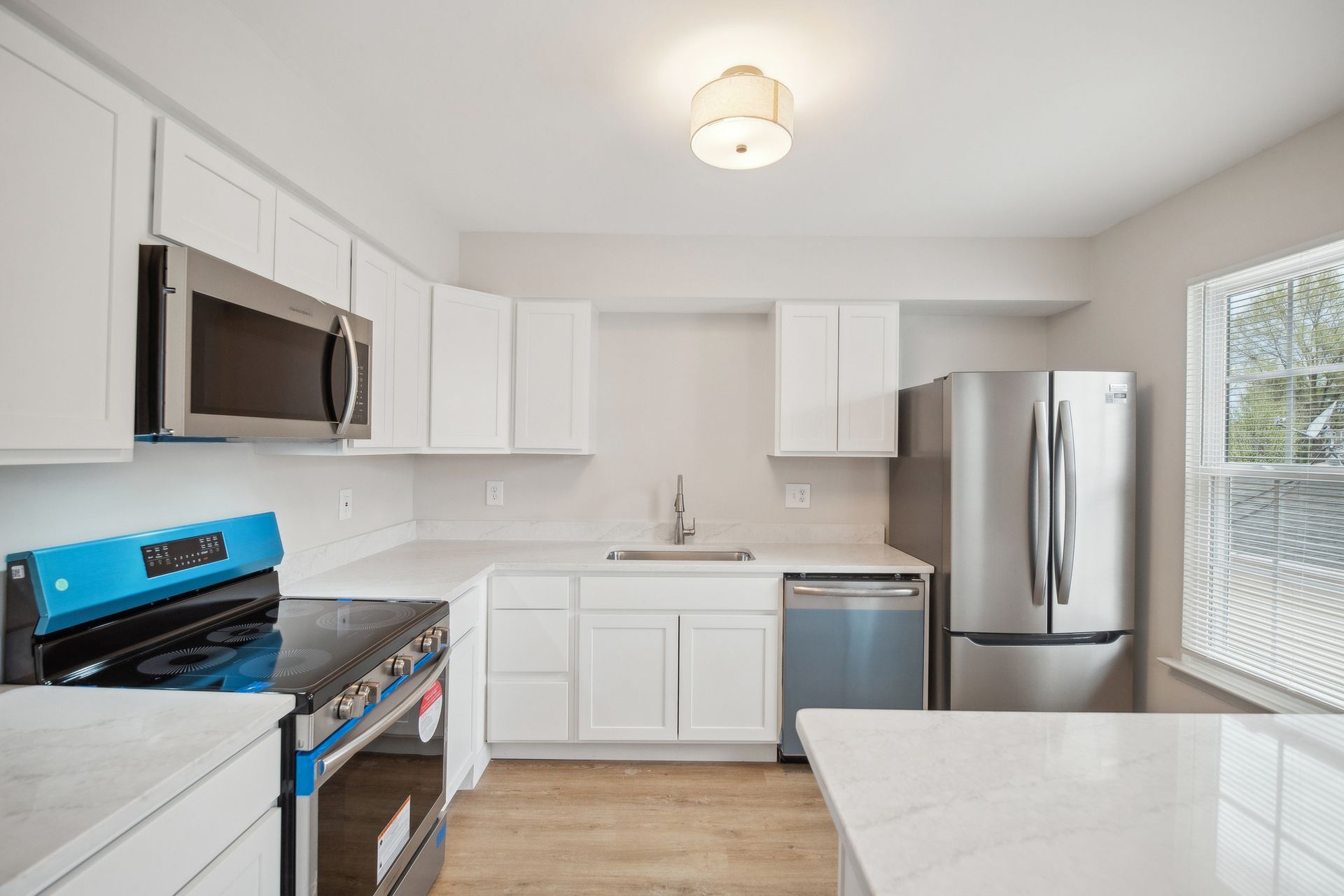 Bright, white kitchen with stainless steel appliances, light countertops, and blue stovetop.