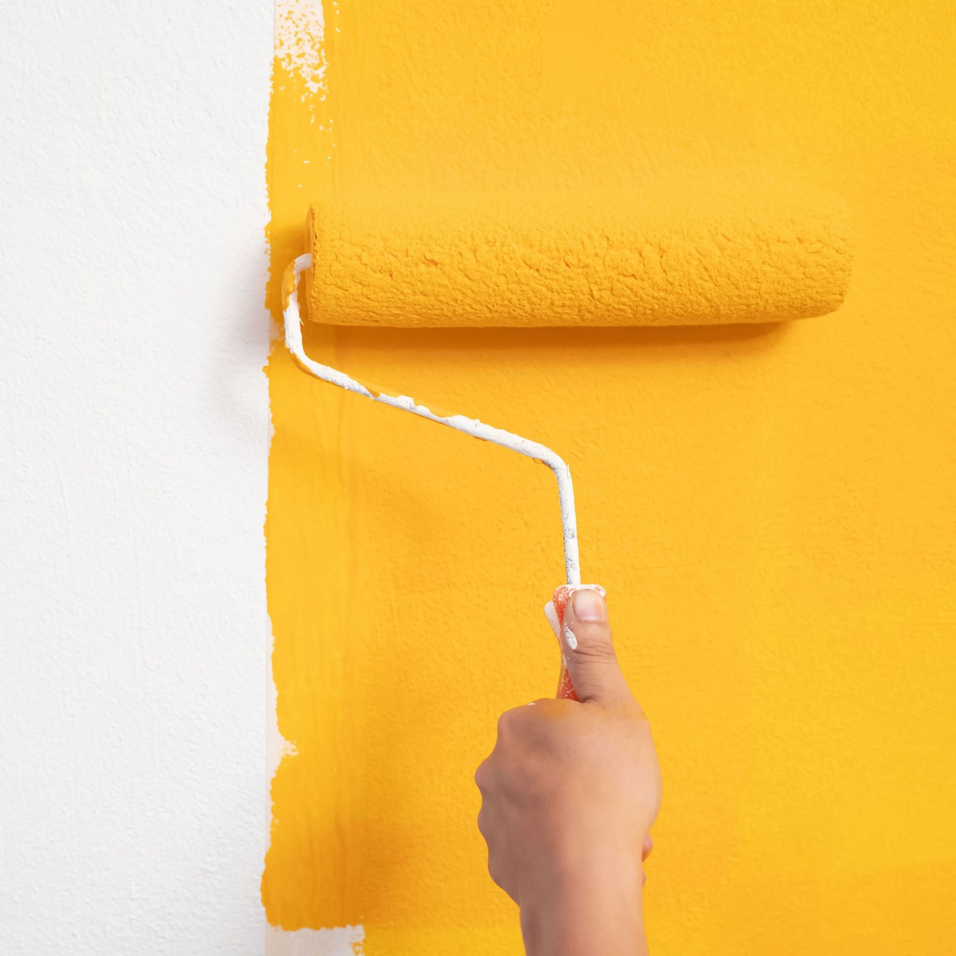 Hand painting a white wall with a yellow paint roller.