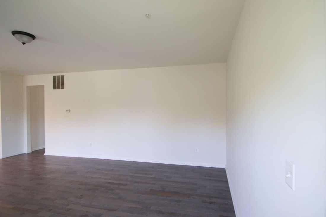 An empty living room with white walls and brown floors