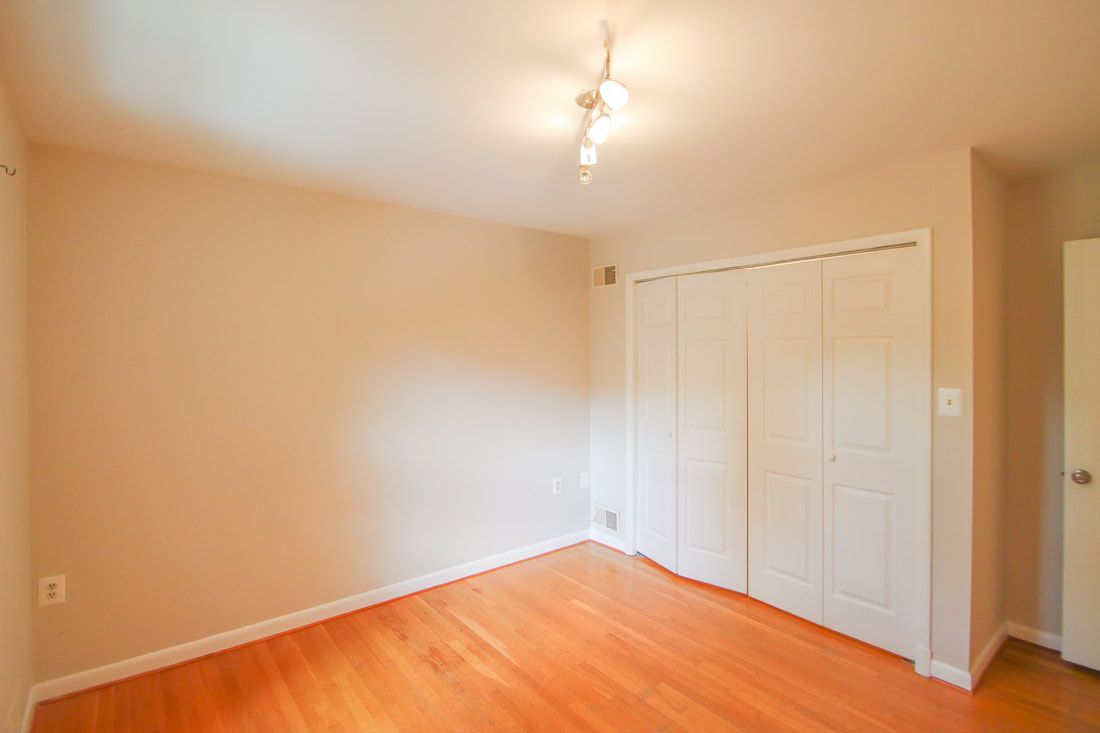 An empty bedroom with hardwood floors and white walls.