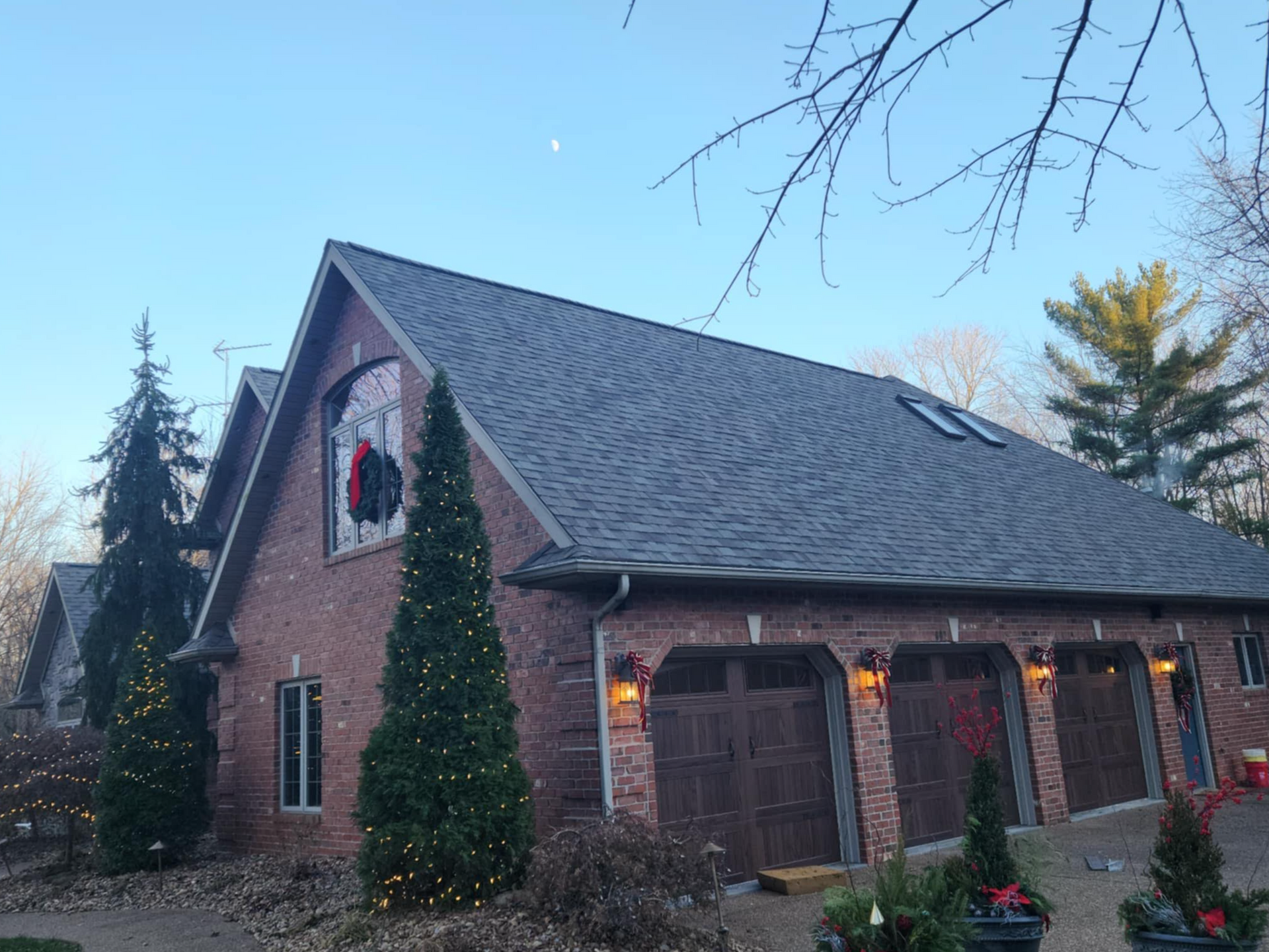 A brick house with three garage doors and christmas trees in front of it