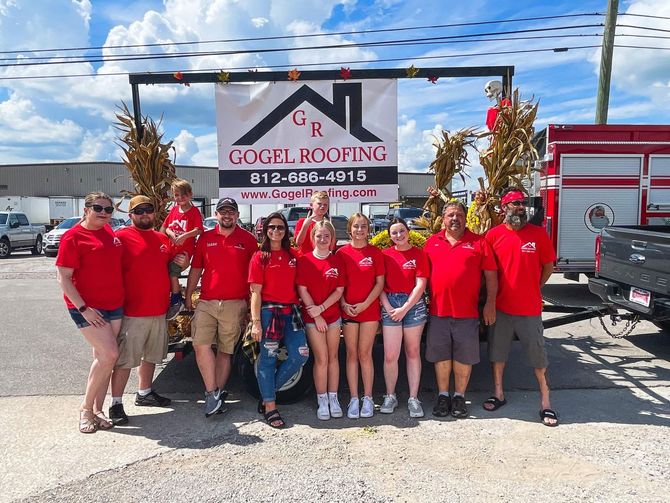 A group of people are posing for a picture in front of a gogel roofing sign.