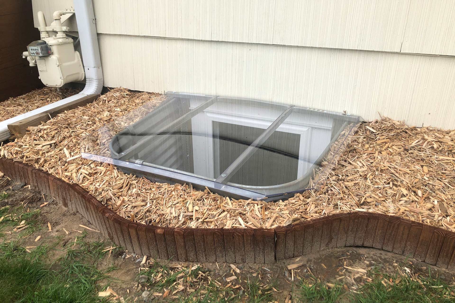 A window well in the ground next to a house.