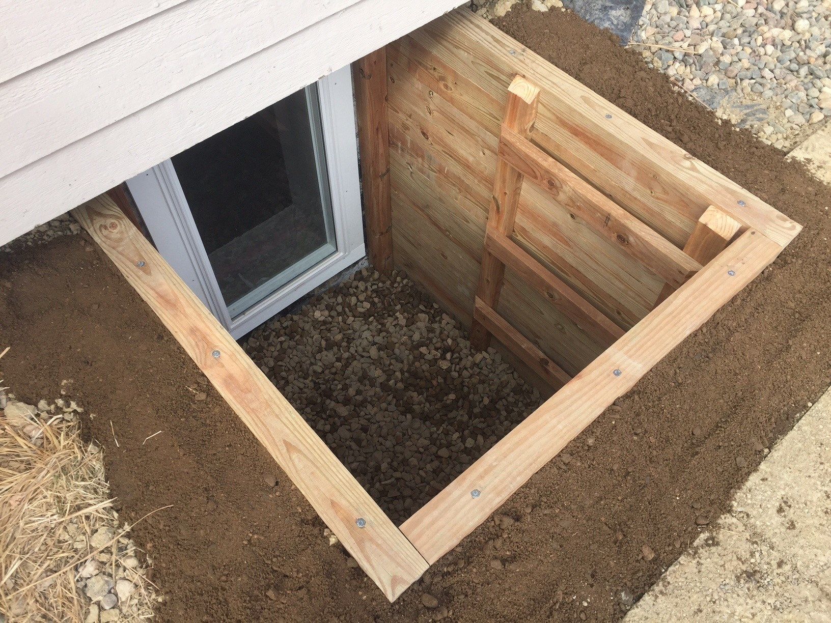 A window well under a house with a wooden frame around it.
