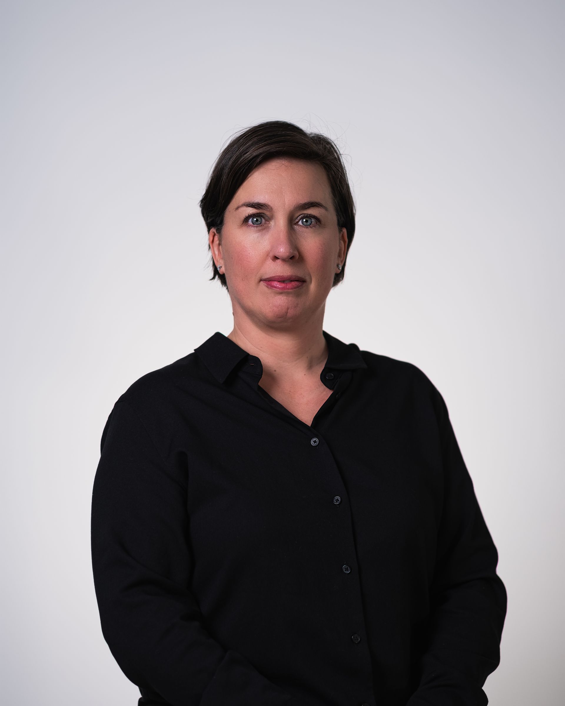 Une femme vêtue d'une chemise noire se tient devant un fond blanc