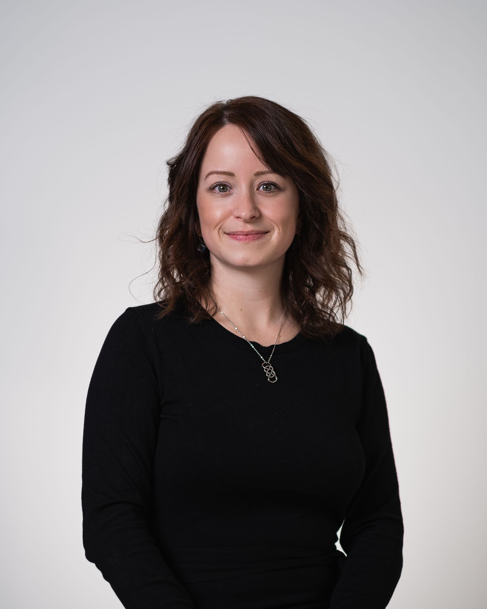 Une femme portant un pull noir et un collier sourit à la caméra.