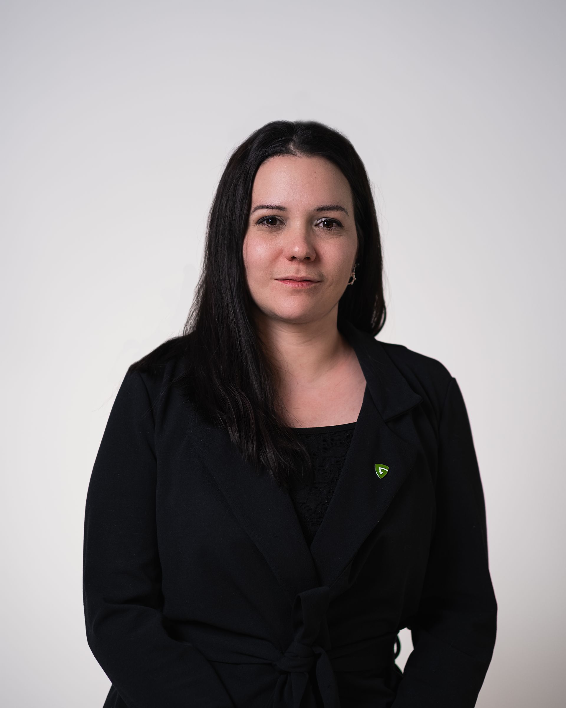 Une femme vêtue d'une veste noire se tient devant un fond blanc.