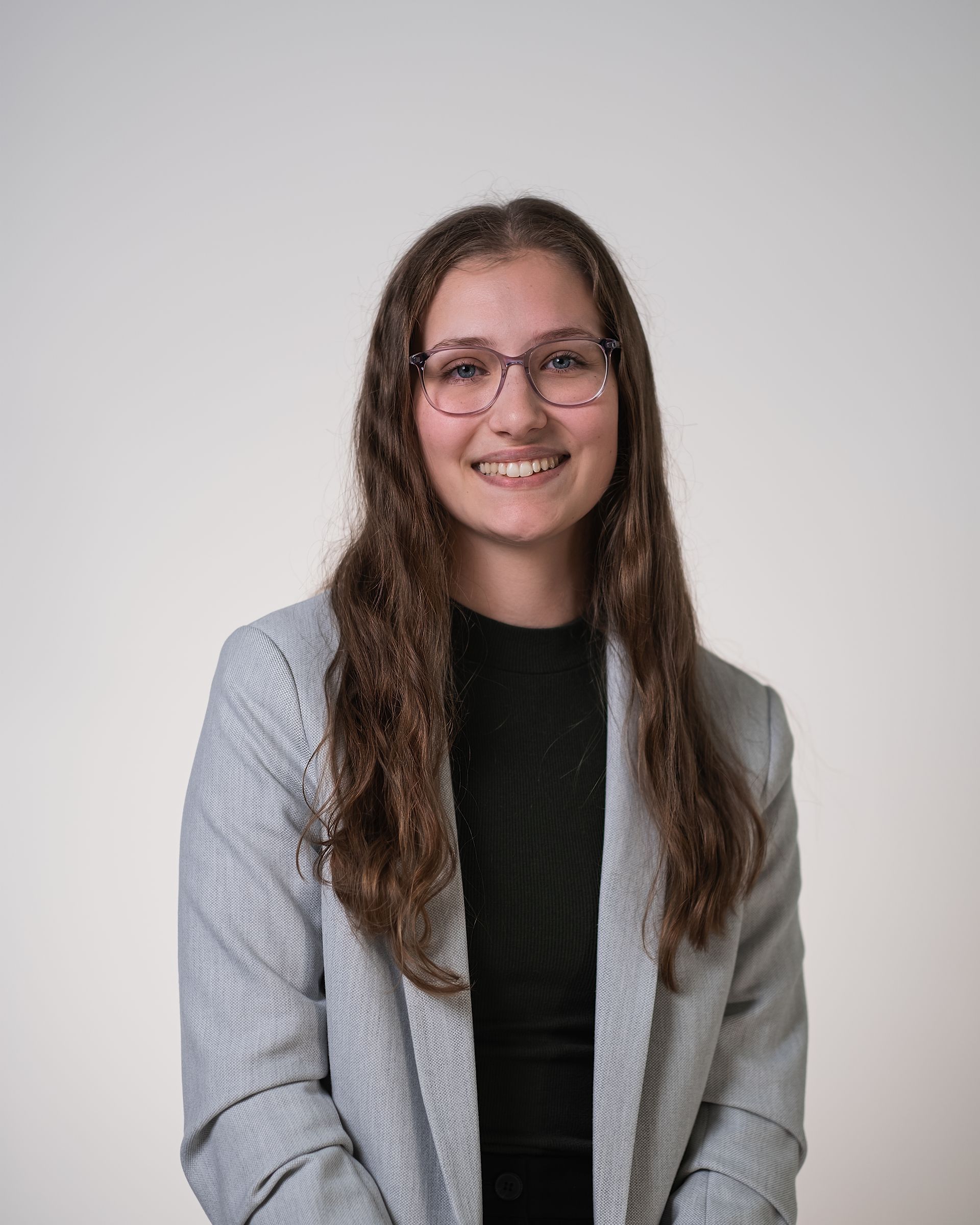 Une jeune femme portant des lunettes et une veste grise sourit à la caméra.