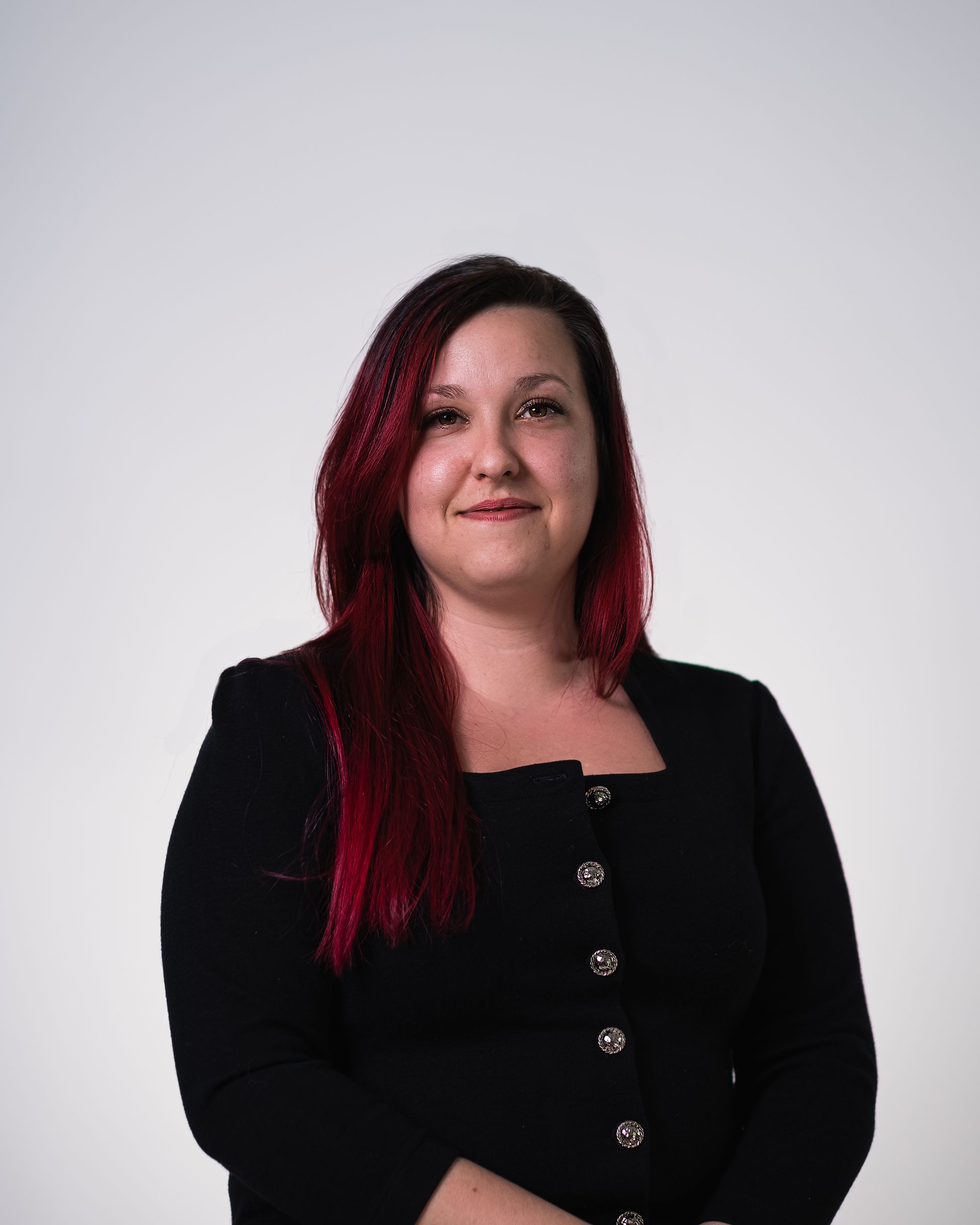 Une femme aux cheveux rouges porte une veste noire et sourit.